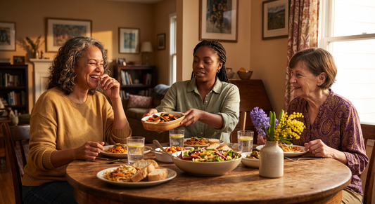 Three women of different ages sharing a casual meal together at a round wooden table in warm afternoon light