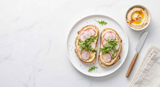 Overhead flat lay of hummus toast topped with radish and arugula on a marble counter