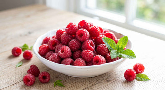 Fresh organic raspberries in a white ceramic bowl with scattered berries and mint